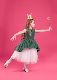 Cute girl in fairy dress with golden crown and magic wand on pink background. Little princess