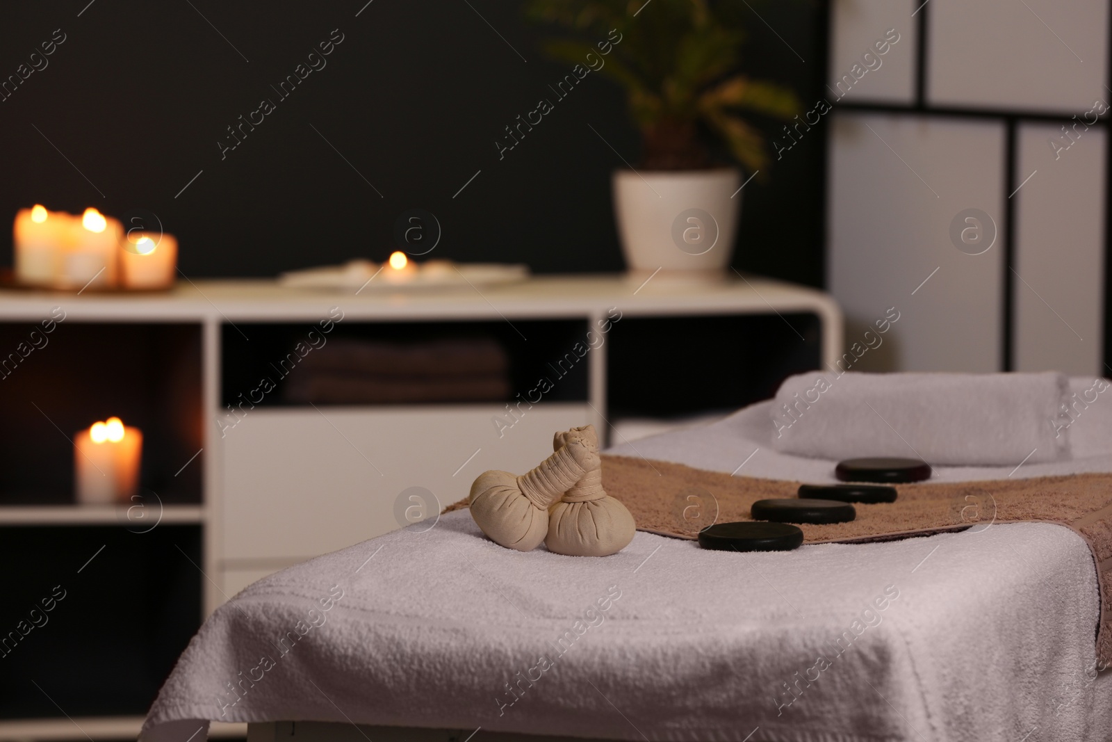 Photo of Herbal compresses and stones on massage table in spa salon