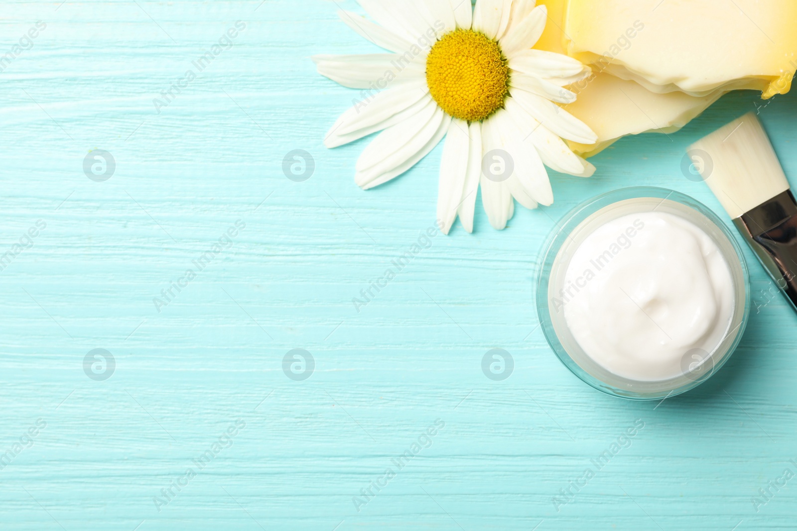 Photo of Jar of cream, soap, brush and chamomile on light blue wooden table, flat lay. Space for text