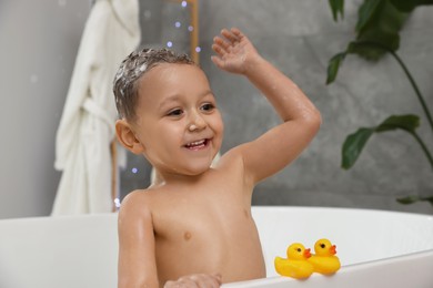 Photo of Cute little boy washing hair with shampoo in bathroom