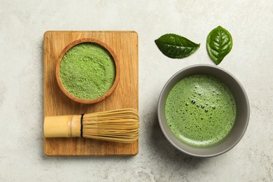 Cup of fresh matcha tea, green powder and bamboo whisk on light grey table, flat lay