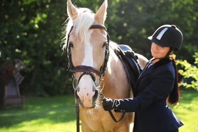 Photo of Young woman in horse riding suit and her beautiful pet outdoors on sunny day