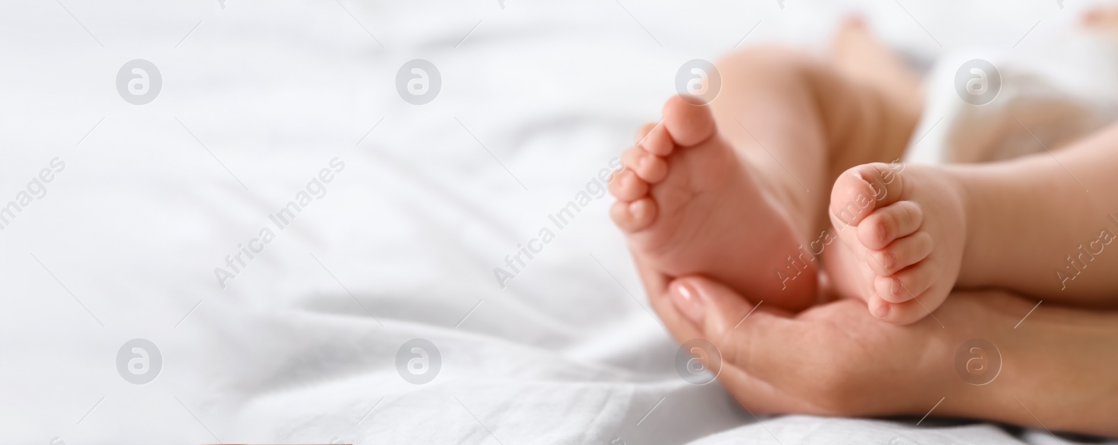 Image of Mother holding feet of her little baby on bed, space for text. Banner design