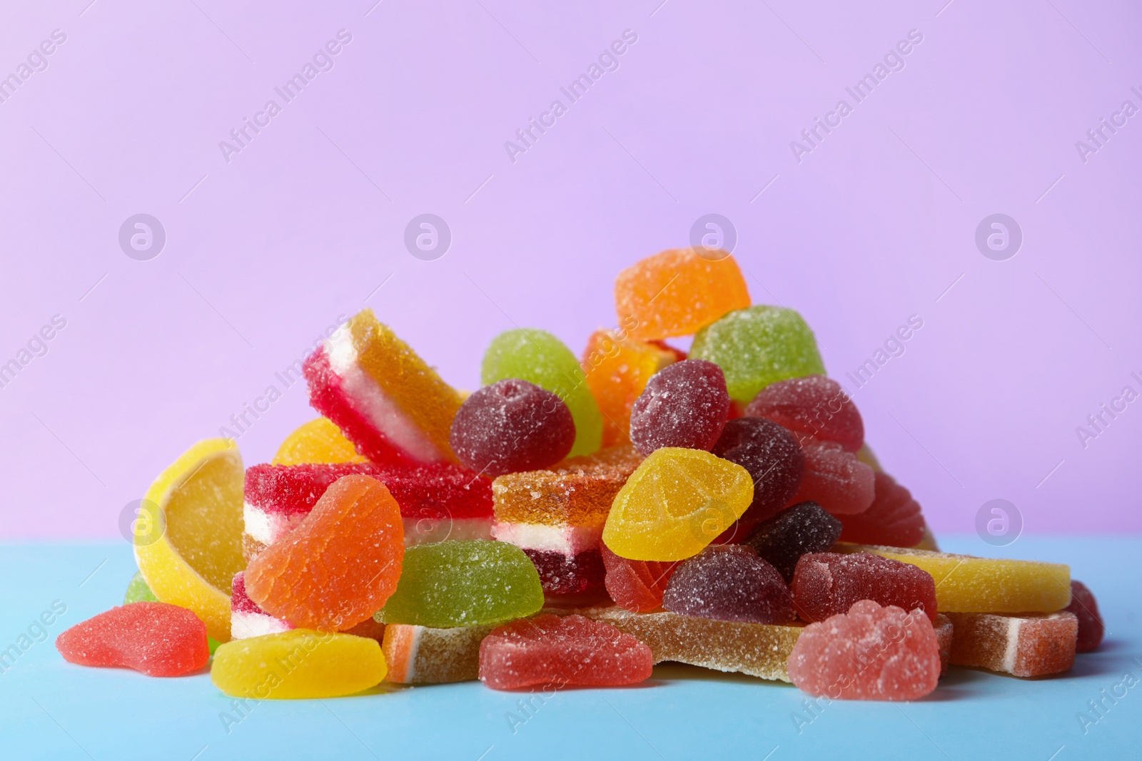 Photo of Pile of delicious bright jelly candies on violet background