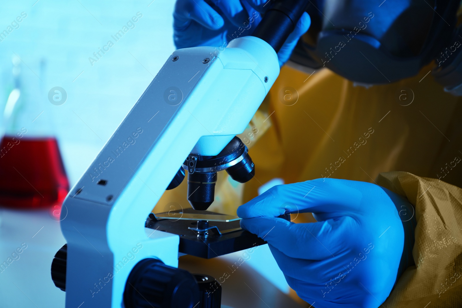 Photo of Scientist in chemical protective suit using microscope at table, closeup. Virus research