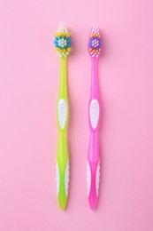 Photo of Colorful plastic toothbrushes on pink background, flat lay