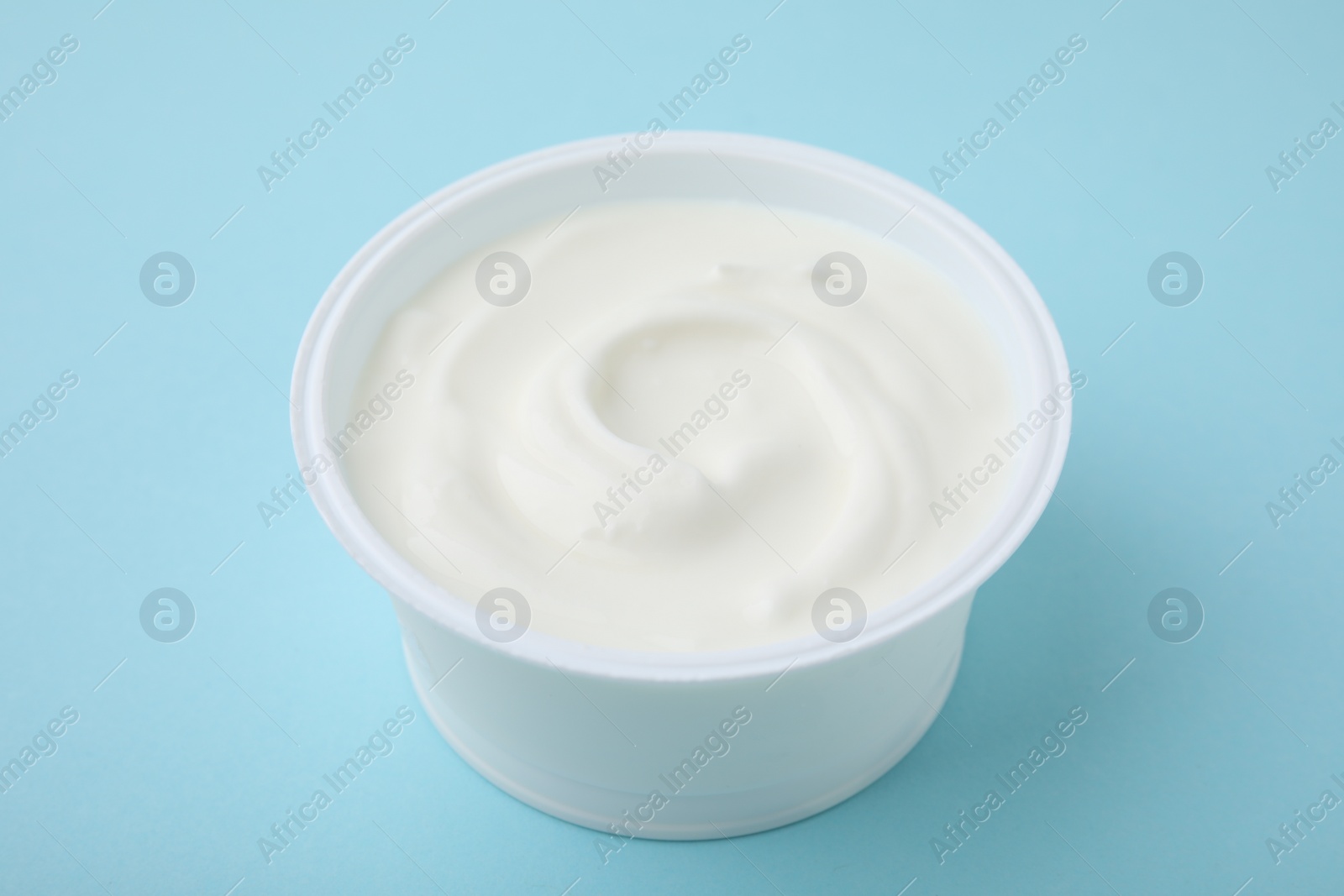 Photo of Delicious natural yogurt in plastic cup on light blue background