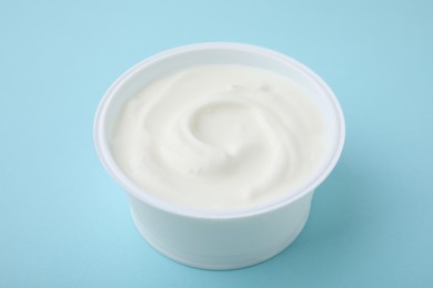 Photo of Delicious natural yogurt in plastic cup on light blue background