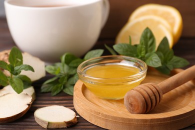 Photo of Bowl with honey for tea, lemon, mint and ginger on wooden table