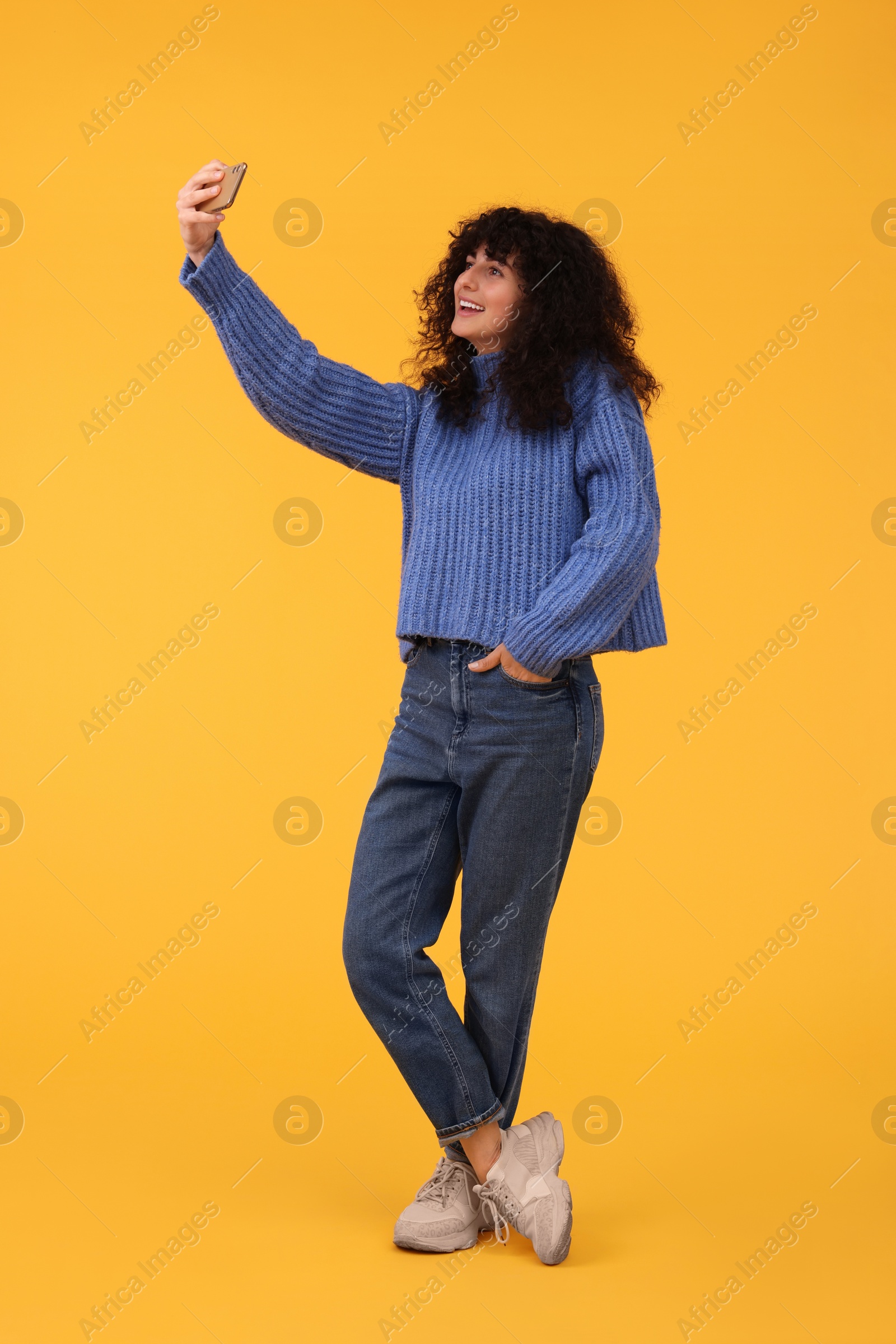 Photo of Beautiful young woman taking selfie with smartphone on orange background