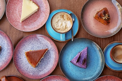 Plates with different cakes and aromatic coffee on wooden table, top view