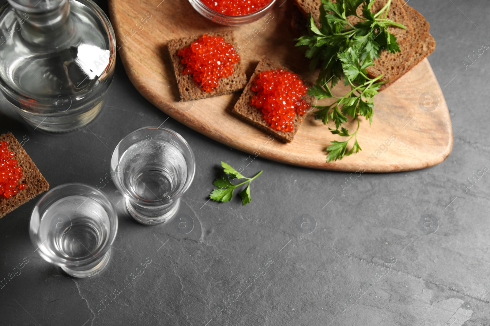 Photo of Cold Russian vodka and sandwiches with red caviar on black table, above view