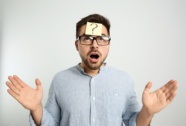 Photo of Emotional man with question mark sticker on forehead against light background