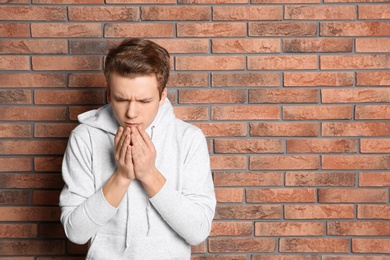 Photo of Teenage boy suffering from cough near brick wall. Space for text