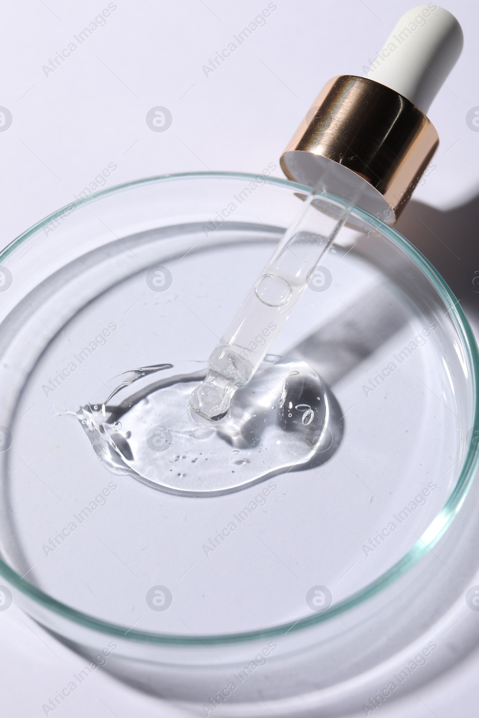Photo of Petri dish with sample of cosmetic serum and pipette on white background, closeup