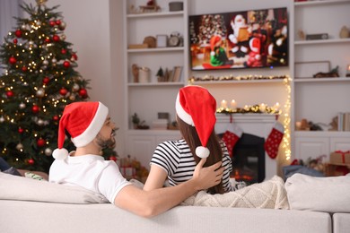 Photo of Happy couple watching Christmas movie via TV in cosy room, back view. Winter holidays atmosphere