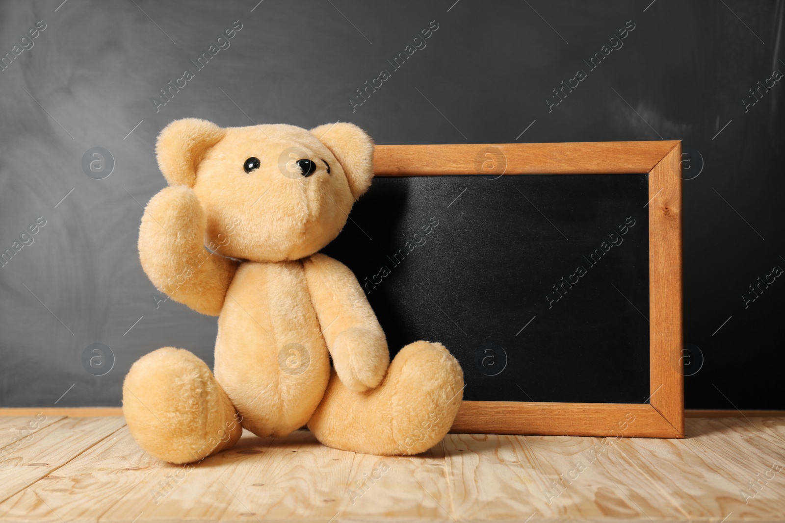 Photo of Teddy bear and small blackboard on wooden table. Space for text