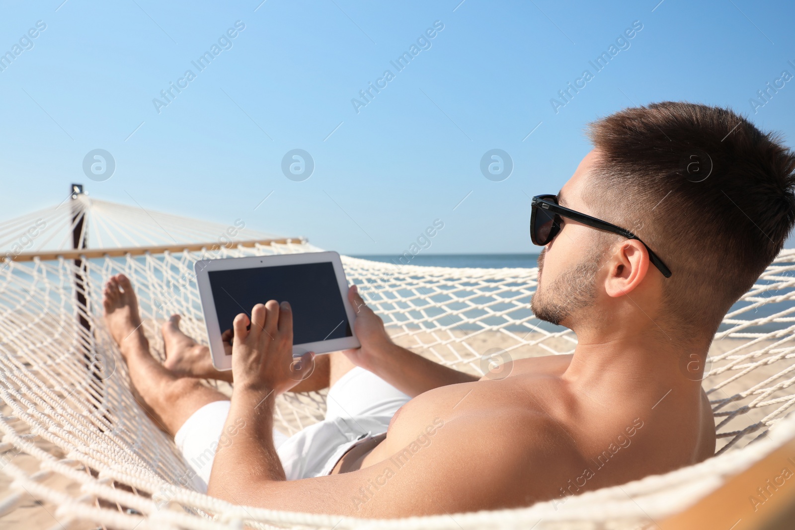 Photo of Young man with tablet in hammock on beach