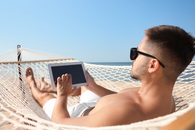 Photo of Young man with tablet in hammock on beach