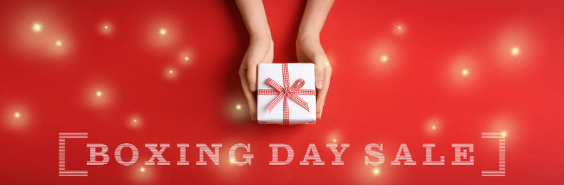 Image of Boxing day sale banner design. Woman holding gift on red background, top view