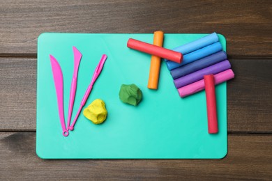 Photo of Many different colorful plasticine pieces with tools on wooden table, top view