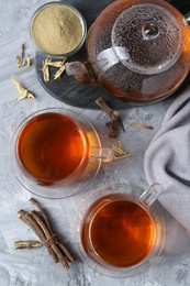 Photo of Aromatic licorice tea, dried sticks of licorice root and powder on light gray textured table, flat lay