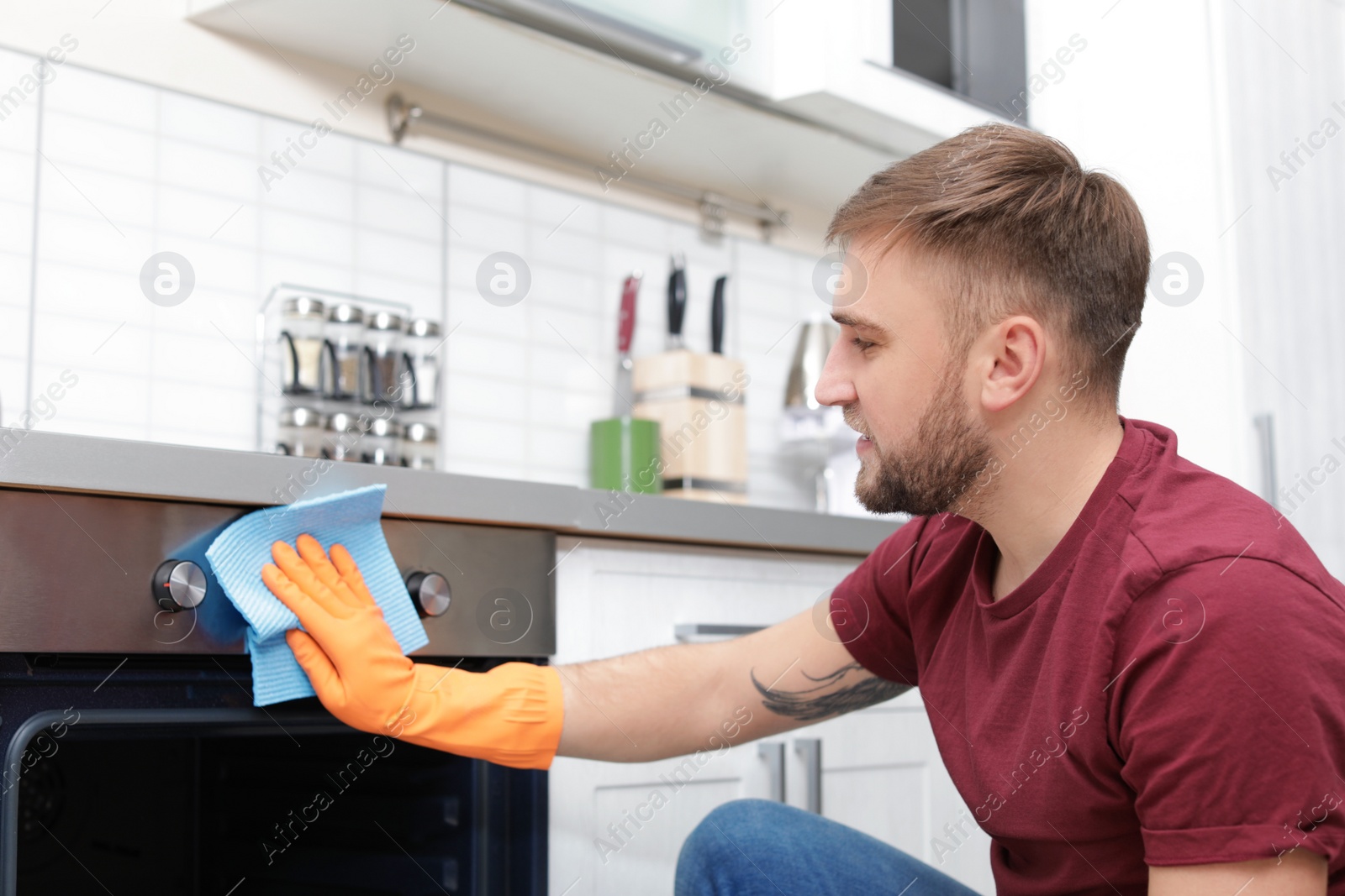 Photo of Young man cleaning oven with rag in kitchen