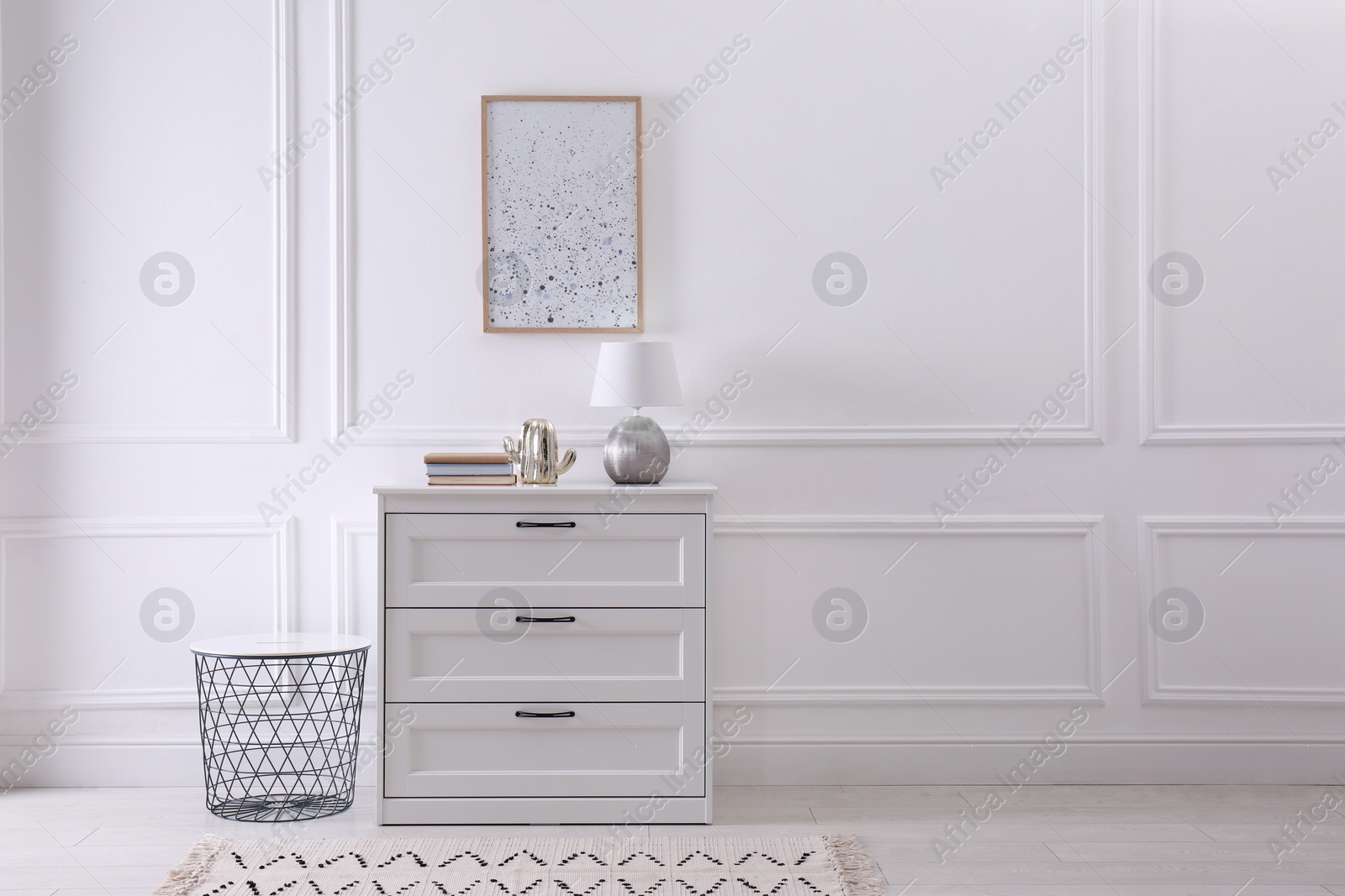 Photo of Wooden chest of drawers with books and lamp near white wall in room, space for text. Interior design