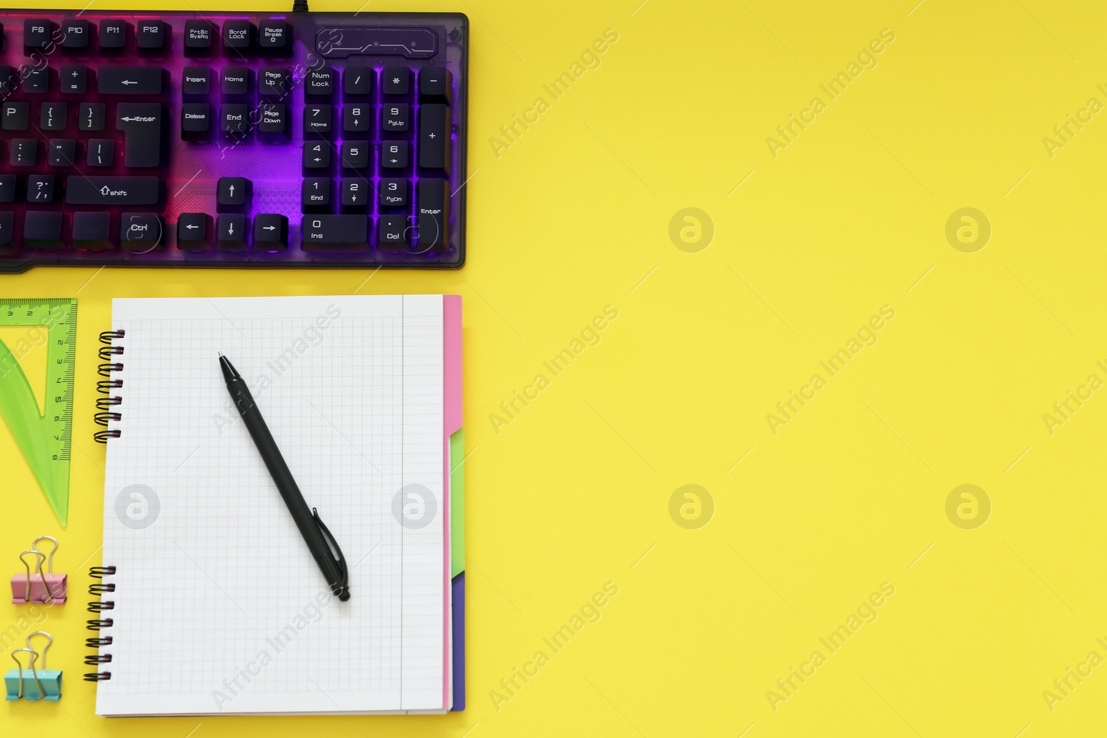 Photo of Modern RGB keyboard and office stationery on yellow background, flat lay. Space for text