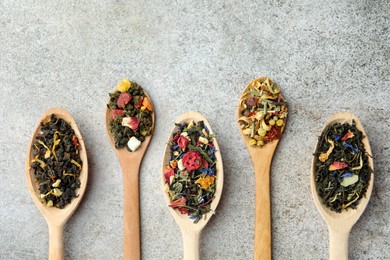 Photo of Different kinds of dry herbal tea in wooden spoons on light grey table, flat lay