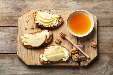 Toasted bread with tasty cream cheese and pear on wooden table, flat lay