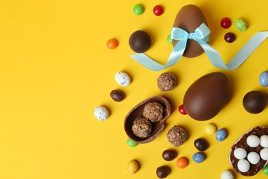 Tasty chocolate eggs and candies on yellow background, flat lay. Space for text