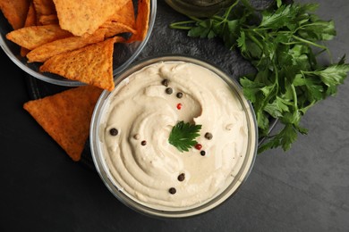 Delicious hummus with nachos and parsley on black table, top view