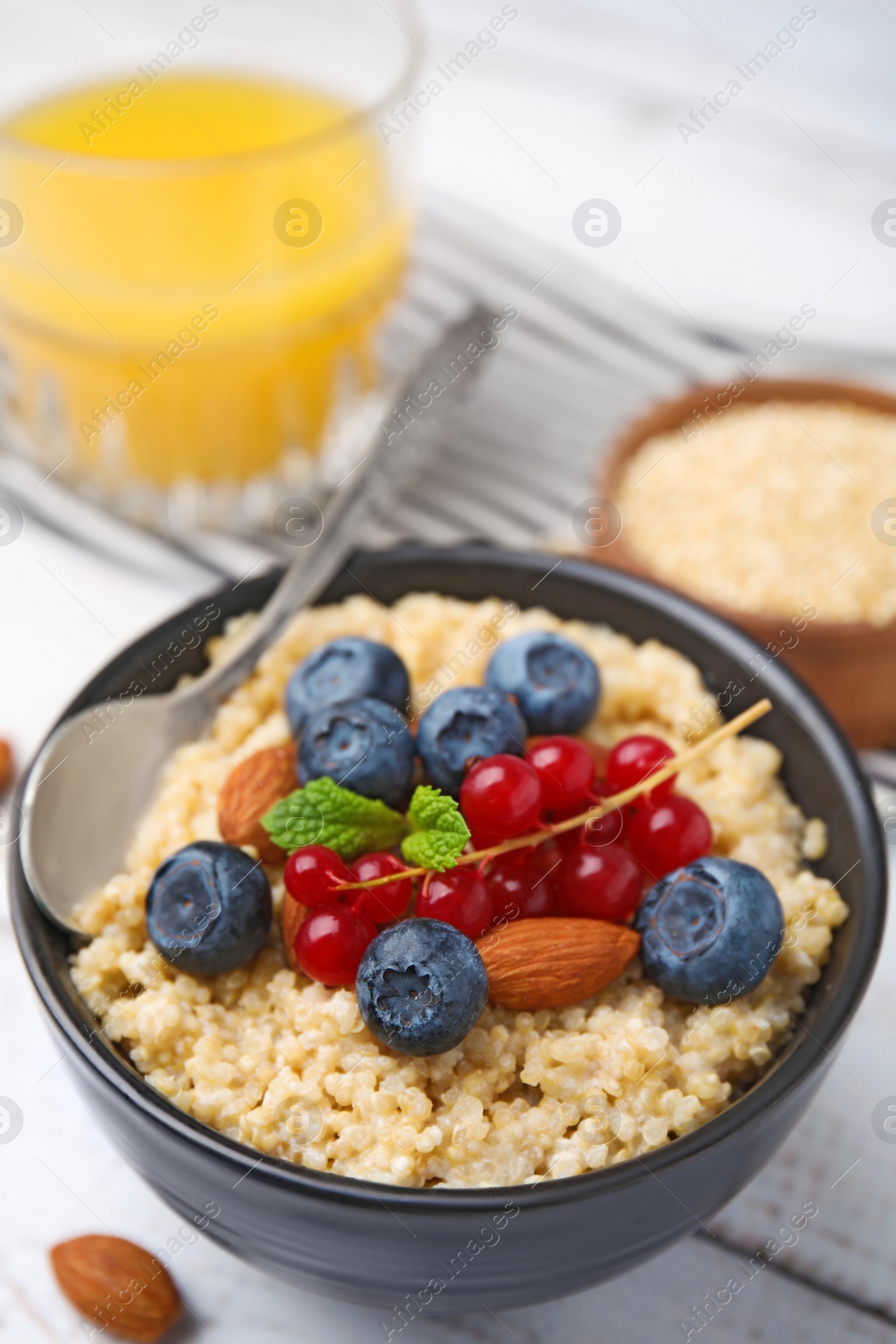 Photo of Bowl of delicious cooked quinoa with almonds, cranberries and blueberries on white wooden table, closeup