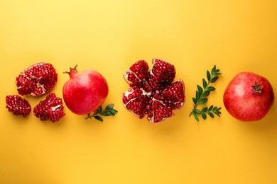 Photo of Fresh pomegranates and green leaves on yellow background, flat lay