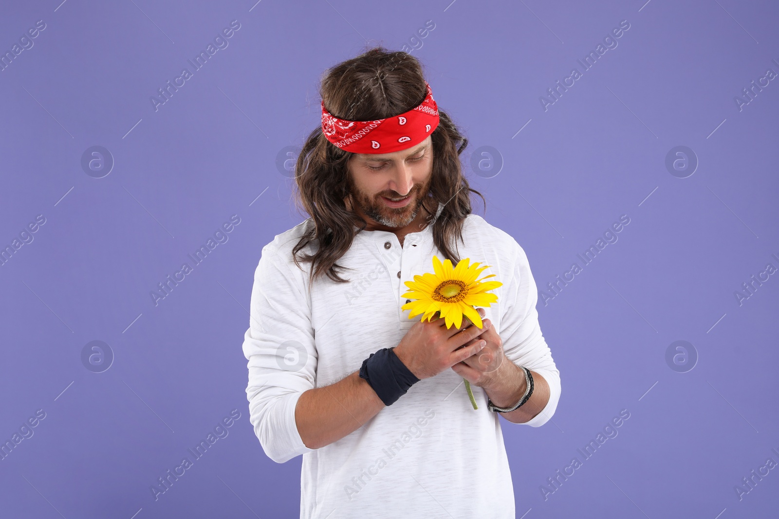 Photo of Stylish hippie man with sunflower on violet background