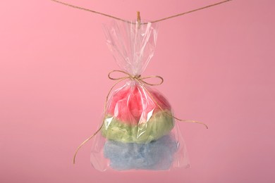 Photo of Packaged sweet cotton candy hanging on clothesline against pink background