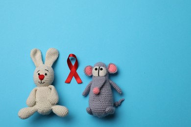 Photo of Cute knitted toys and red ribbon on blue background, flat lay with space for text. AIDS disease awareness