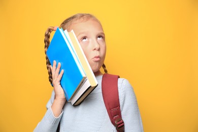Funny little girl with backpack and textbooks on yellow background. Space for text