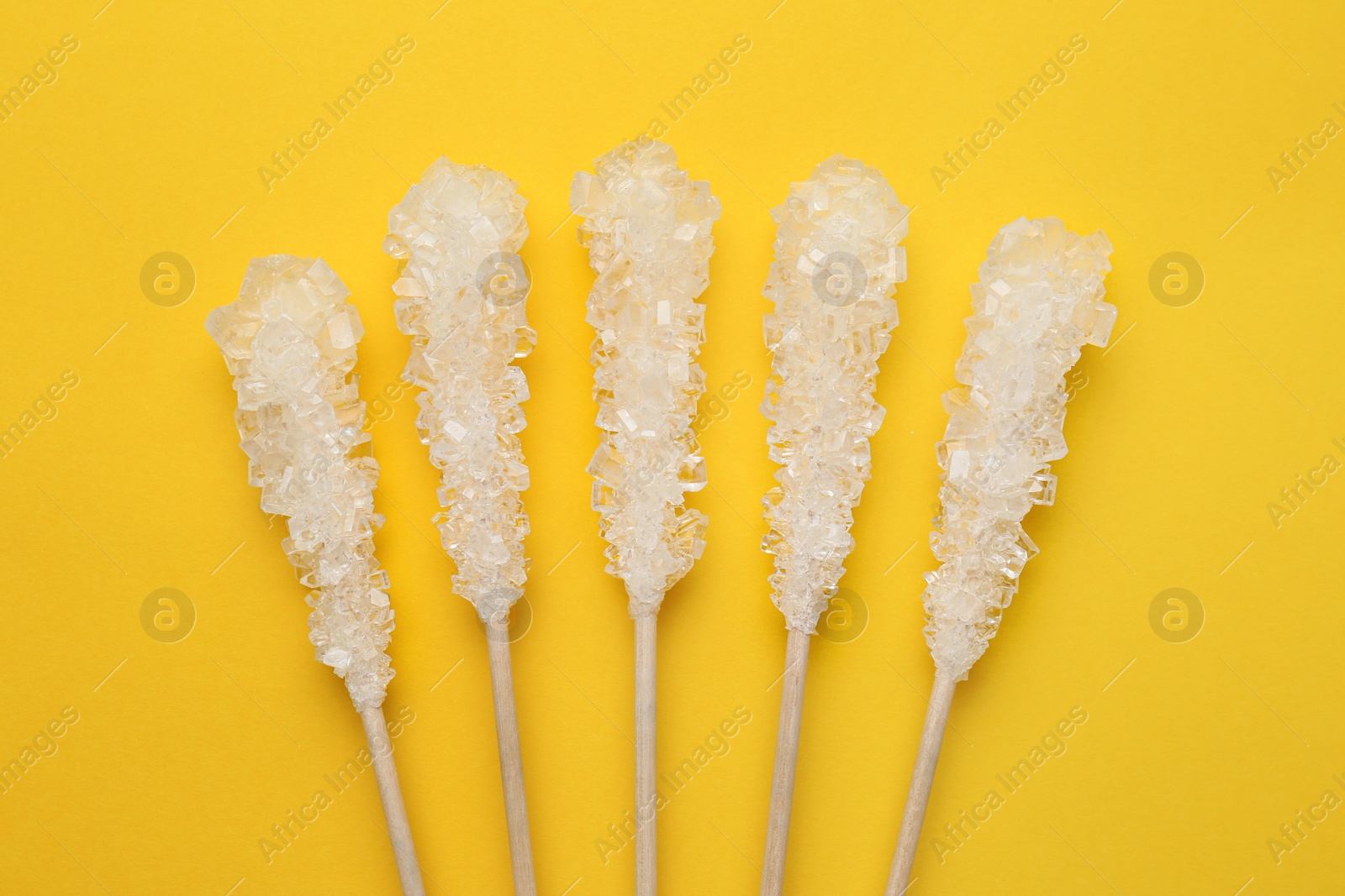 Photo of Wooden sticks with sugar crystals on yellow background, flat lay. Tasty rock candies