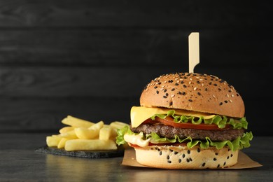 Photo of Burger with delicious patty and french fries on gray table against dark background, space for text