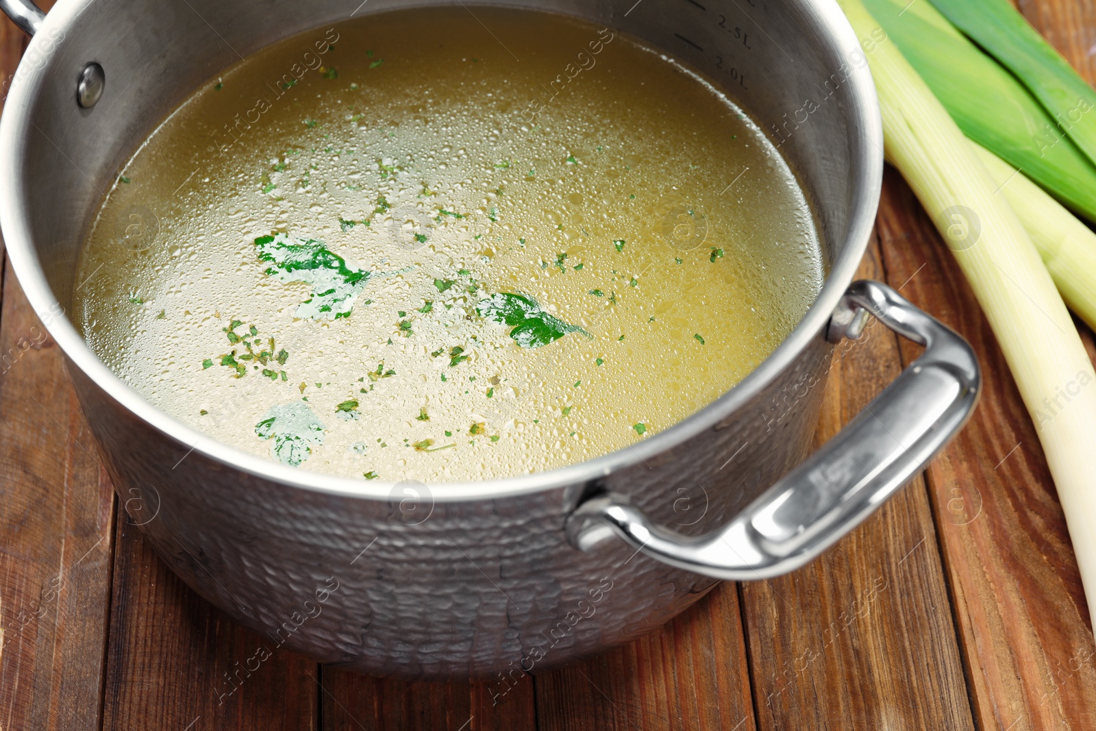 Photo of Pot with tasty bouillon and celery on wooden table, closeup