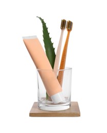 Photo of Tube of toothpaste, brushes and aloe vera leaf in glass on white background