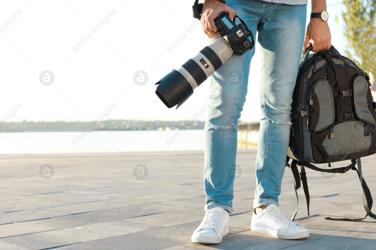 Photo of Young male photographer holding professional camera and backpack at pier. Space for text