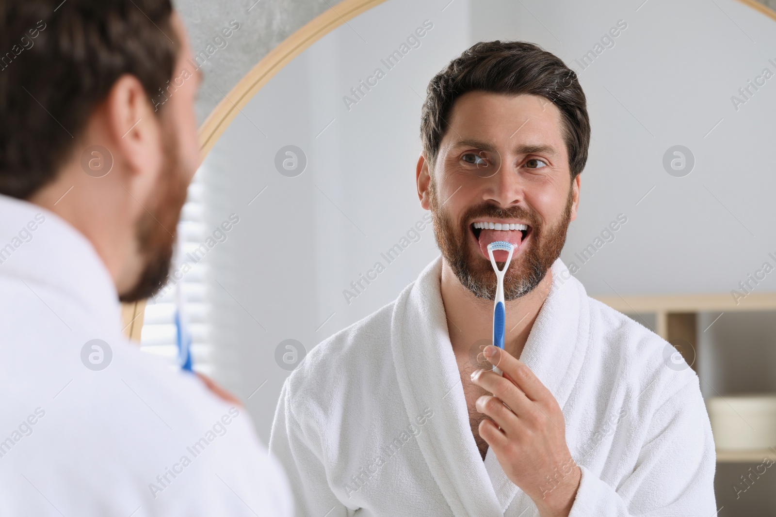 Photo of Handsome man brushing his tongue with cleaner near mirror in bathroom
