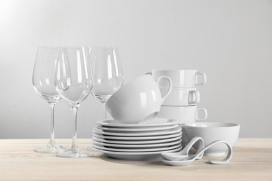Photo of Set of clean dishware and glasses on white wooden table against light background