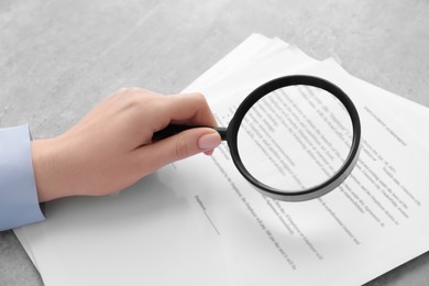 Photo of Woman looking at document through magnifier at light gray table, closeup. Searching concept