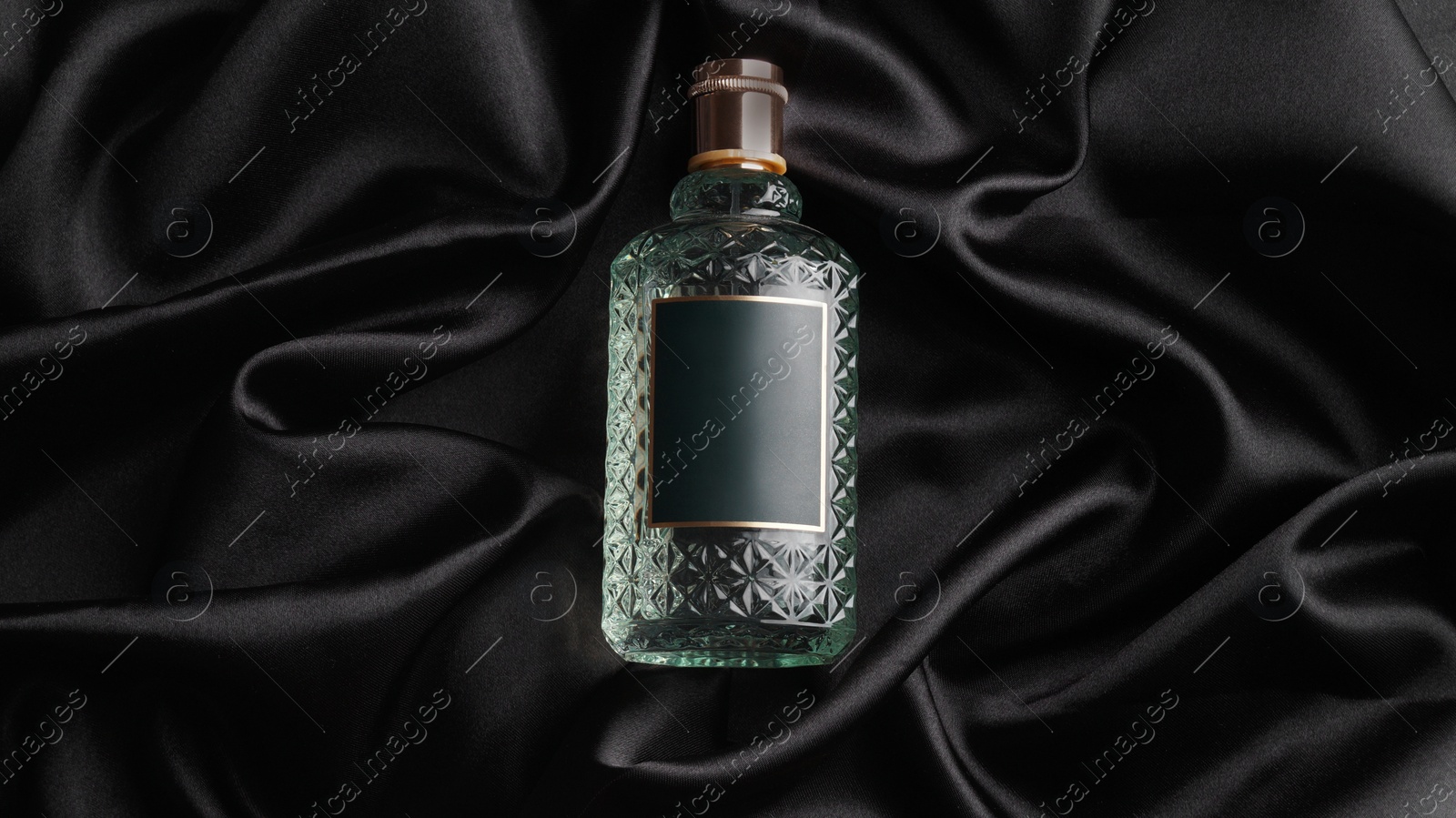 Photo of Luxury bottle of perfume on black silk, top view