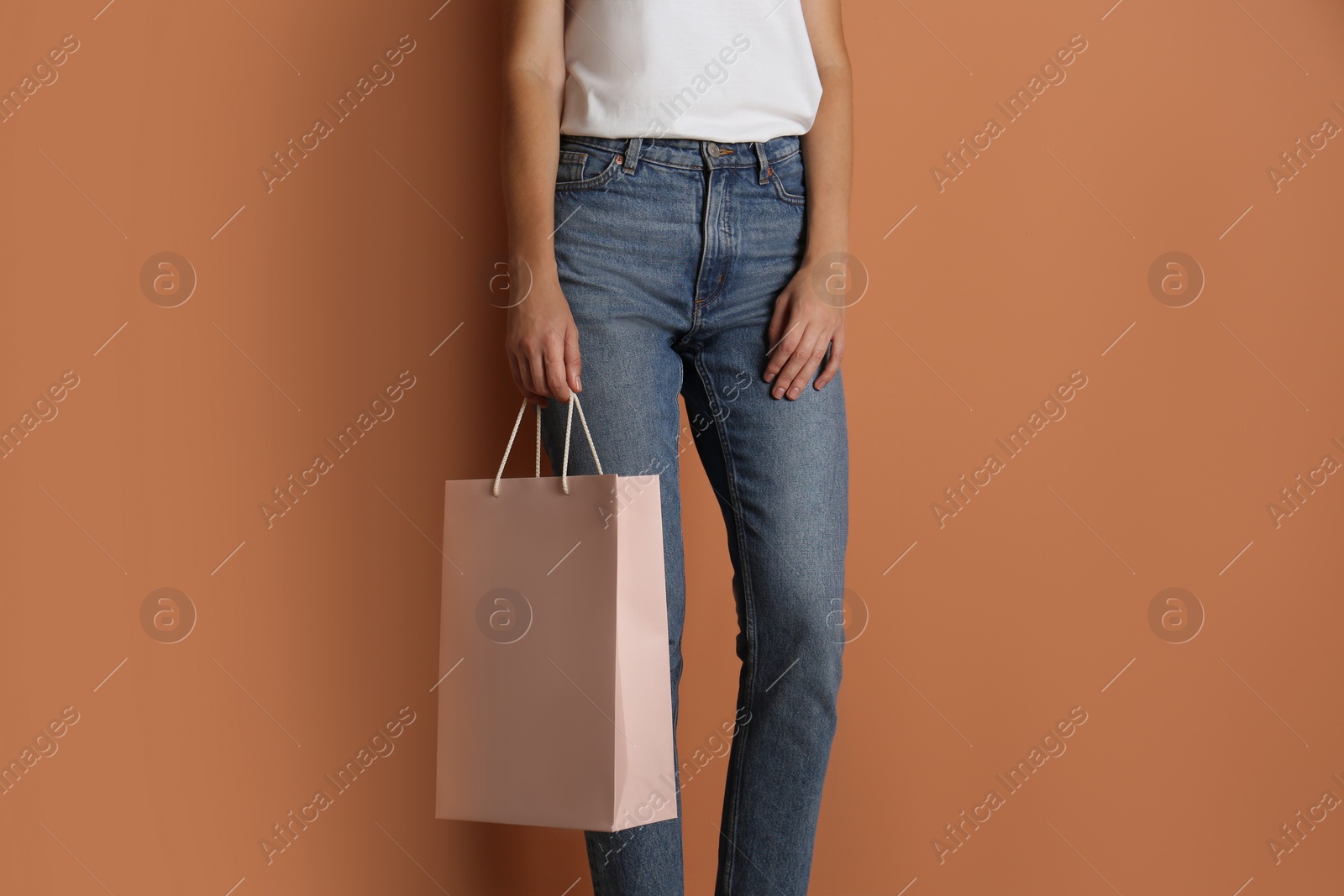 Photo of Woman with paper shopping bag on light brown background, closeup