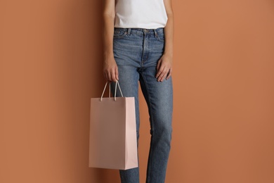 Woman with paper shopping bag on light brown background, closeup